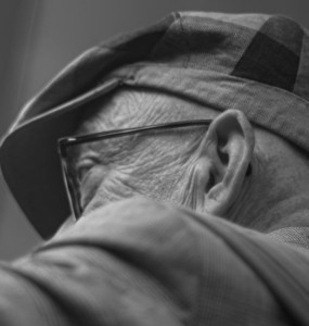 An elderly man wears a hat and glasses.