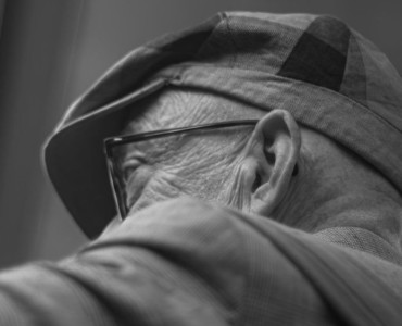 An elderly man wears a hat and glasses.