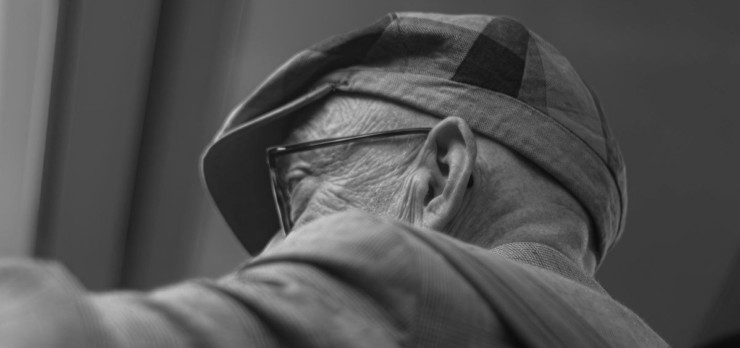 An elderly man wears a hat and glasses.