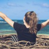 woman in black shirt sitting on brown wooden log near body of water during daytime