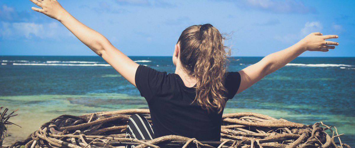 woman in black shirt sitting on brown wooden log near body of water during daytime