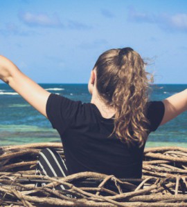 woman in black shirt sitting on brown wooden log near body of water during daytime
