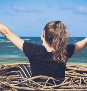 woman in black shirt sitting on brown wooden log near body of water during daytime