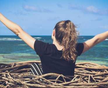 woman in black shirt sitting on brown wooden log near body of water during daytime