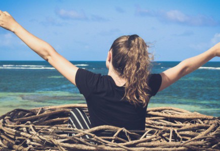 woman in black shirt sitting on brown wooden log near body of water during daytime