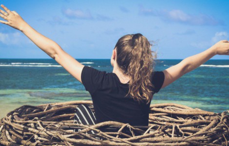 woman in black shirt sitting on brown wooden log near body of water during daytime