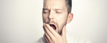 Close-up of a bearded man yawning with hand on mouth against a white background.