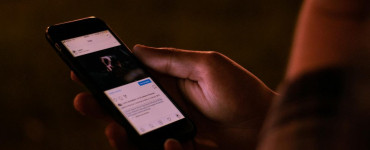 A person interacts with a smartphone in a dimly lit setting, emphasizing mobile technology usage.