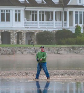 Serene scene of a man fishing in front of a grand lakeside mansion.