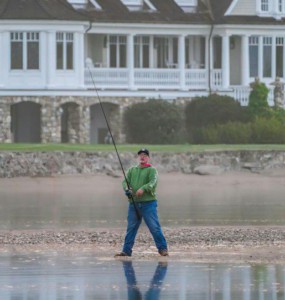 Serene scene of a man fishing in front of a grand lakeside mansion.