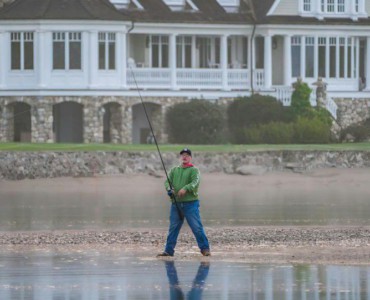 Serene scene of a man fishing in front of a grand lakeside mansion.