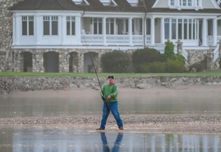 Serene scene of a man fishing in front of a grand lakeside mansion.
