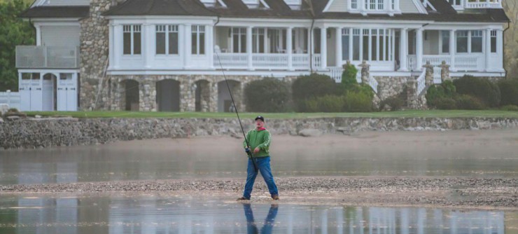 Serene scene of a man fishing in front of a grand lakeside mansion.