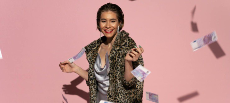 Stylish woman in fur coat with flying euro notes and pink background. Bright, fashionable, and confident.