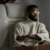 A stylish man in a turtleneck relaxes inside a private jet, embodying luxury travel.