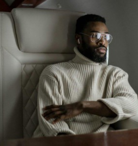 A stylish man in a turtleneck relaxes inside a private jet, embodying luxury travel.