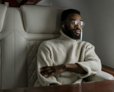 A stylish man in a turtleneck relaxes inside a private jet, embodying luxury travel.