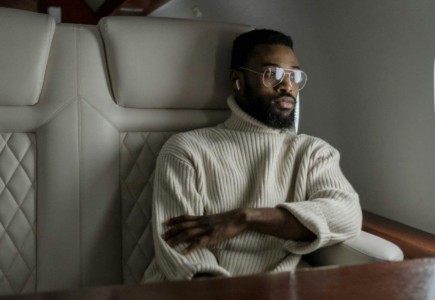 A stylish man in a turtleneck relaxes inside a private jet, embodying luxury travel.