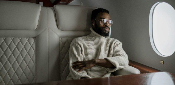 A stylish man in a turtleneck relaxes inside a private jet, embodying luxury travel.