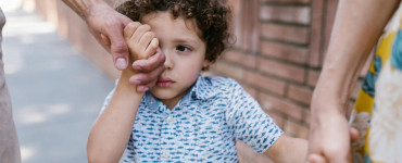 A little boy with curly hair holds hands with family in a close-up outdoor scene.