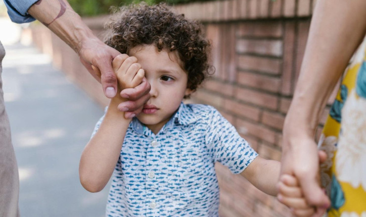 A little boy with curly hair holds hands with family in a close-up outdoor scene.