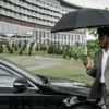 African American man in a suit walking by a car under an umbrella on a rainy day.