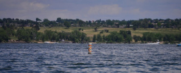 A tranquil scene of a buoy floating in a serene Colorado lake, against a lush green backdrop.