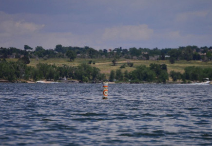 A tranquil scene of a buoy floating in a serene Colorado lake, against a lush green backdrop.
