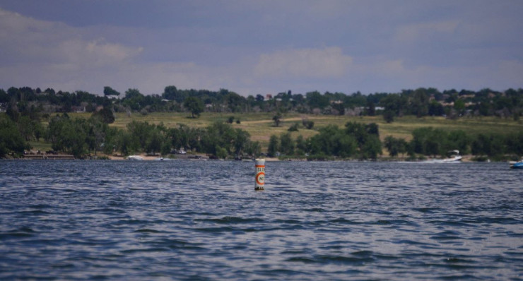 A tranquil scene of a buoy floating in a serene Colorado lake, against a lush green backdrop.