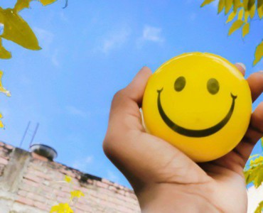 a hand holding a yellow smiley face ball