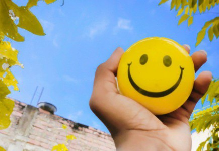 a hand holding a yellow smiley face ball