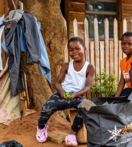 Two smiling children in front of a wooden house.
