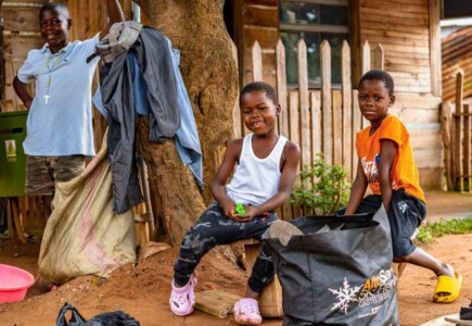 Two smiling children in front of a wooden house.