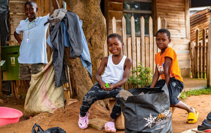 Two smiling children in front of a wooden house.