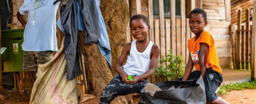 Two smiling children in front of a wooden house.