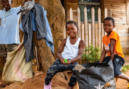 Two smiling children in front of a wooden house.