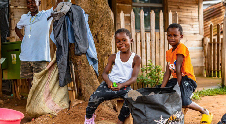 Two smiling children in front of a wooden house.
