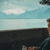man sitting while holding a book watching on body of water