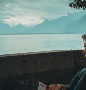 man sitting while holding a book watching on body of water