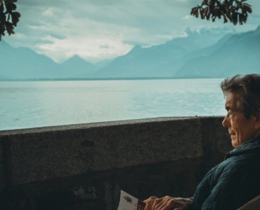 man sitting while holding a book watching on body of water