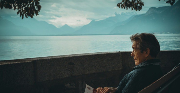 man sitting while holding a book watching on body of water