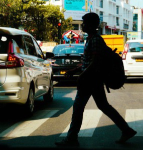 People crossing a busy city street with cars.