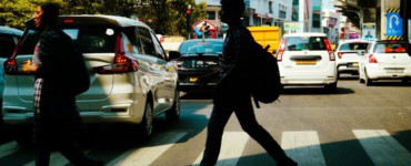 People crossing a busy city street with cars.