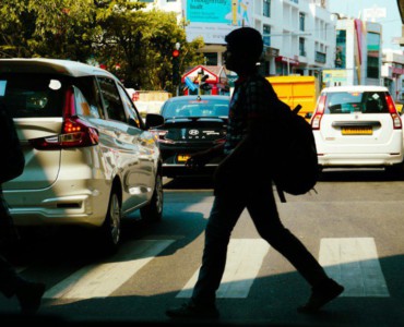 People crossing a busy city street with cars.
