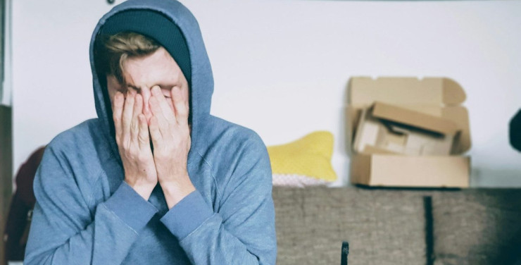 man covering face with both hands while sitting on bench